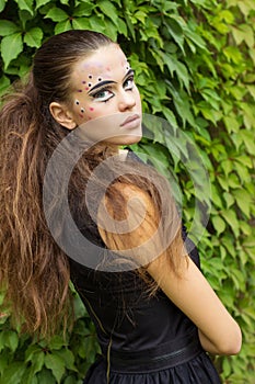 Beautiful young girl on the background of the leaves in autumn day on the street with fantasy makeup in a black dress