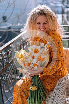 Beautiful young girl on the balcony of the house rejoices at a bouquet of spring flowers, daffodils.