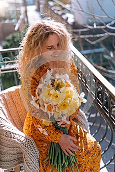 Beautiful young girl on the balcony of the house rejoices at a bouquet of spring flowers, daffodils. Spring time.