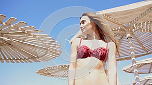 Beautiful young girl in a bathing suit stands on the beach umbrellas and looks away