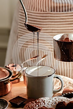 Beautiful young girl in beige apron is preparing delicious organic hot chocolate in old vintage ladle. Soft daylight, lifestyle