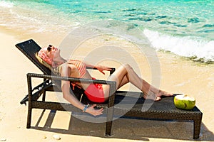 Beautiful young girl in bikini is lying on a sun lounger coast o