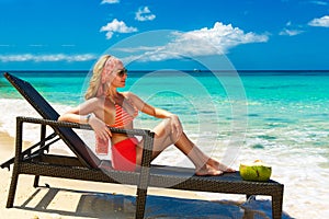 Beautiful young girl in bikini is sitting on a sun lounger coast