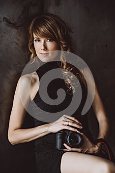 Beautiful young girl in a black dress with a camera in her hands in a loft studio. Soft selective focus. Woman photographer