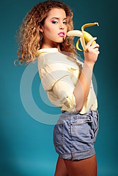 Beautiful young girl with blond hair and bright makeup with banana