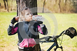 Beautiful young girl with blond hair drinking water on the go while cycling