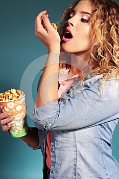Beautiful young girl with blond hair and evening makeup eating popcorn