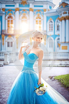 Beautiful young girl in a blue ball gown walking through the palace park