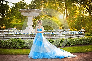 Beautiful young girl in a blue ball gown walking through the palace park