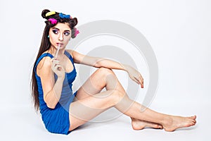 Beautiful young girl in blue dress with curlers sits on the floor and chews the cud.