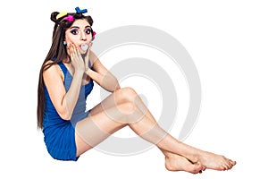 Beautiful young girl in blue dress with curlers sits on the floor and chews the cud.