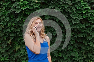 Beautiful young girl in a blue dress talking on the phone. Against the background of wild grapes, summer day. Copy space