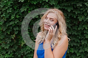 Beautiful young girl in a blue dress talking on the phone. Against the background of wild grapes, summer day. Copy space