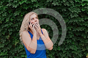 Beautiful young girl in a blue dress talking on the phone. Against the background of wild grapes, summer day. Copy space