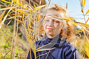 A beautiful, beautiful and young girl in a blue sweater is smiling in the reeds on the bank of the river, her hair backlit by the