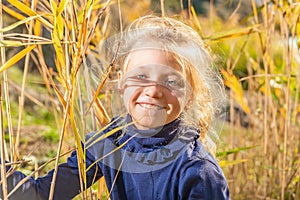 A beautiful, beautiful and young girl in a blue sweater is smiling in the reeds on the bank of the river, her hair backlit by the