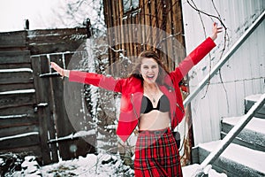 Girl in a bra, red skirt and leather jacket walks around the yard near the old building and laughs