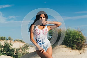 beautiful young girl in a bright bathing suit posing on a white beach, model raised her hand to her neck, slightly