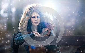 Beautiful young girl with brown fur cape enjoying the winter scenery sitting on the bench in park. Teenage girl posing, winter