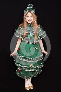 Beautiful young girl in a carnival costume of a Christmas tree smiles on a black background