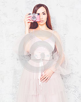 Beautiful young girl in a chic airy pink dress, takes a picture of a vintage pink camera.