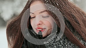 A beautiful young girl with chic long hair is enjoying falling snow in winter. Face close-up.