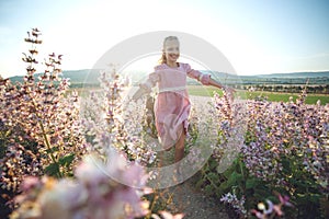 Beautiful young girl child runs across the field with flowers at sunset