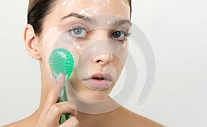 Beautiful young girl cleansing face with cosmetic facial skincare foam, gel or soap by brush