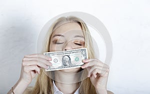 Beautiful young girl with closed eyes sniffing cash, grey background