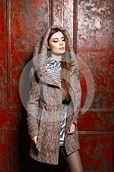 Beautiful young girl in a coat with hood near vintage wall