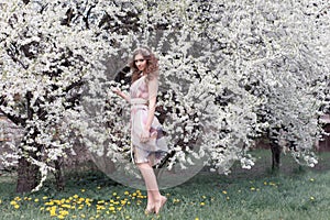 Beautiful young girl with curls in an air colored dress with a wreath on her head walking in the park near a cherry blossom