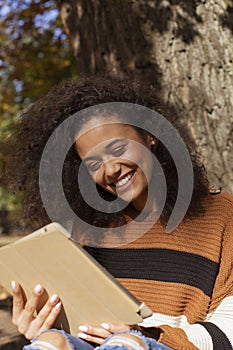 Beautiful young girl with dark curly hair using tablet computer, outdoor.