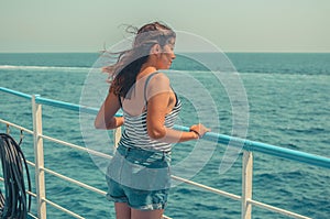 Beautiful young girl with dark hair in a striped t-shirt and blue denim shorts stands on the deck of a ship at sea