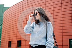 Beautiful young girl with dark hair wearing casual clothes posing near red wall, street style, outdoor portrait, hipster girl in