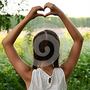 beautiful and young girl depicts a heart with her hands above her head.
