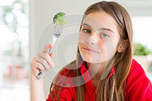 Beautiful young girl eating fresh broccoli with a confident expression on smart face thinking serious