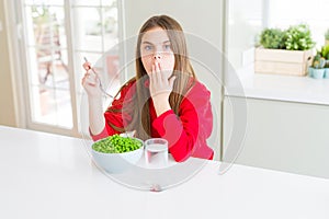 Beautiful young girl eating healthy green peas cover mouth with hand shocked with shame for mistake, expression of fear, scared in