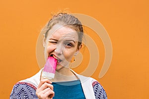 Beautiful and young girl eats a pink hue ice cream and enjoys. She closed her eyes from the cold of the ice cream.