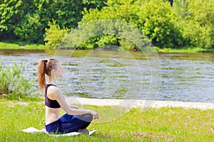 Beautiful young girl is engaged in sports, yoga, fitness on the beach by the river on a Sunny summer day