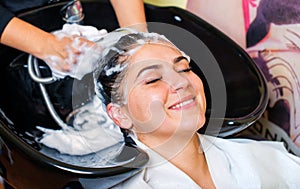 Beautiful young girl enjoying hair washing in hairdressing salon.