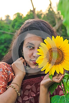 Beautiful young girl enjoying nature on the field of sunflowers. Girl in park smiling and covering face with sunflower.