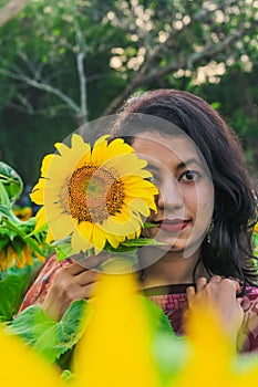 Beautiful young girl enjoying nature on the field of sunflowers. Girl in park smiling and covering face with sunflower.