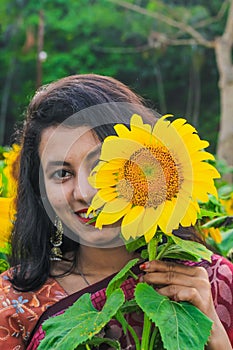 Beautiful young girl enjoying nature on the field of sunflowers. Girl in park smiling and covering face with sunflower.