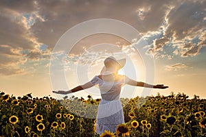 Beautiful young girl enjoying nature on the field of sunflowers at sunset