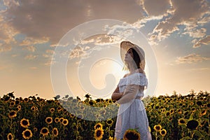 Beautiful young girl enjoying nature on the field of sunflowers at sunset