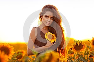 Beautiful young girl enjoying nature on the field of sunflowers at sunset. Summertime. Attractive brunette woman with long healthy