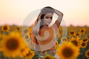 Beautiful young girl enjoying nature on the field of sunflowers at sunset. Summertime. Attractive brunette woman with long healthy