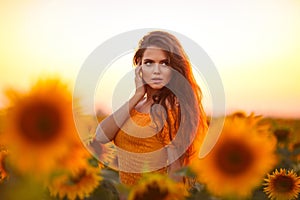 Beautiful young girl enjoying nature on the field of sunflowers at sunset. Summertime. Attractive brunette woman with long healthy