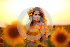 Beautiful young girl enjoying nature on the field of sunflowers at sunset. Summertime. Attractive brunette woman with long healthy