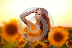 Beautiful young girl enjoying nature on the field of sunflowers at sunset. Summertime. Attractive brunette woman with long healthy